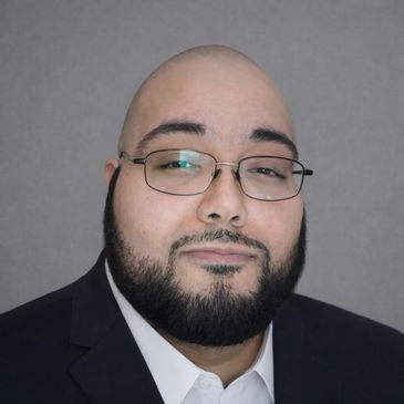 Man with glasses and beard wearing a suit and white shirt.