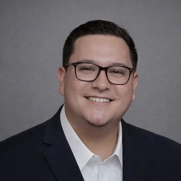 Smiling man wearing glasses and a suit against a plain gray background.