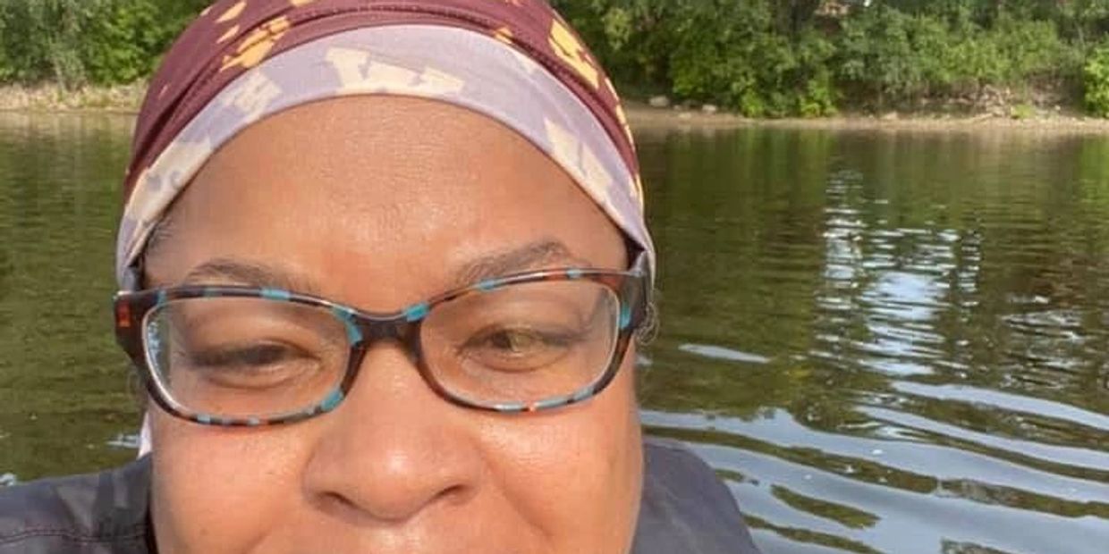 Close-up selfie of a woman wearing glasses and a headscarf near a body of water.