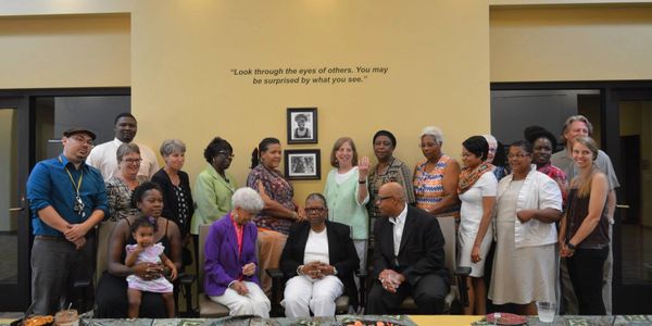 A diverse group of people posing for a photo indoors with a quote on the wall.