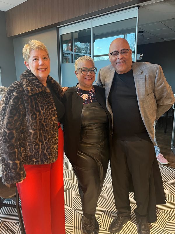 Three adults smiling indoors, dressed in stylish outfits.