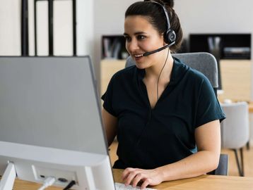 A customer support wearing headset and is in front of her desktop