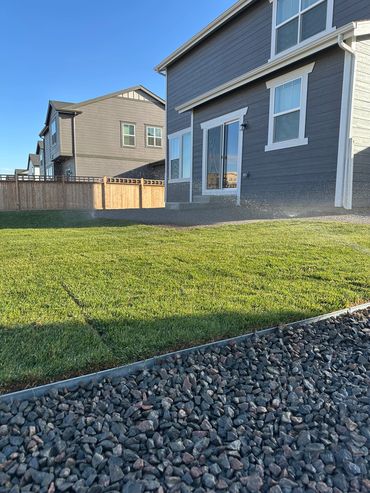Lawn sprinklers watering a backyard with green grass and a gray house.