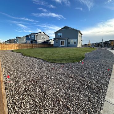 Suburban backyard with green grass and surrounding gravel under a blue sky.