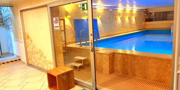 Beheiztes Schwimmbad mit Glaswand und Holzstuhl.