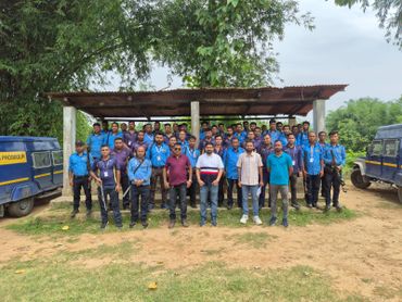 Group photo of security personnel and staff in blue uniforms with two armored vehicles.