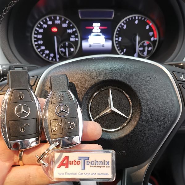 2 Mercedes remote keys shown in front of a steering wheel with an LCD dashboard display background