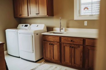Laundry room with white washer, dryer, wooden cabinets, and a sink under a window.