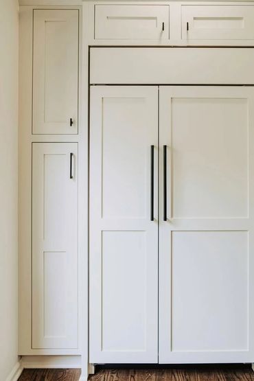 Built-in white kitchen cabinets with black handles and wood flooring.