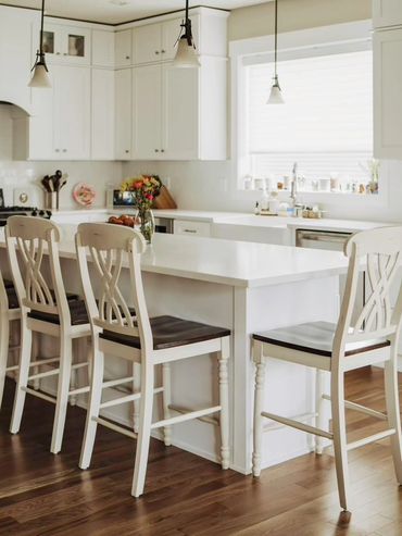 Bright, spacious kitchen with white cabinetry and wooden stools at a large island.