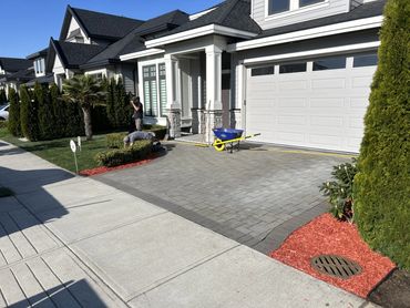 Two workers landscaping a modern house front yard on a sunny day.