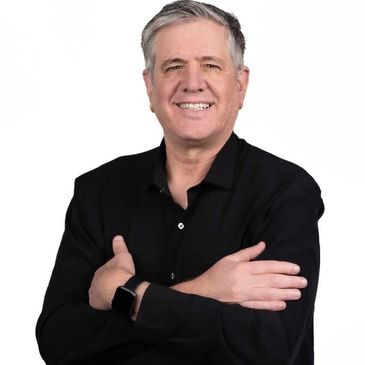 Man in black shirt with arms crossed, smiling confidently.