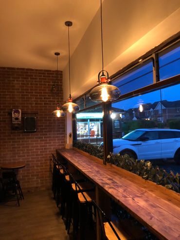 Cozy cafe corner with hanging lights and wooden counter seating by a large window.