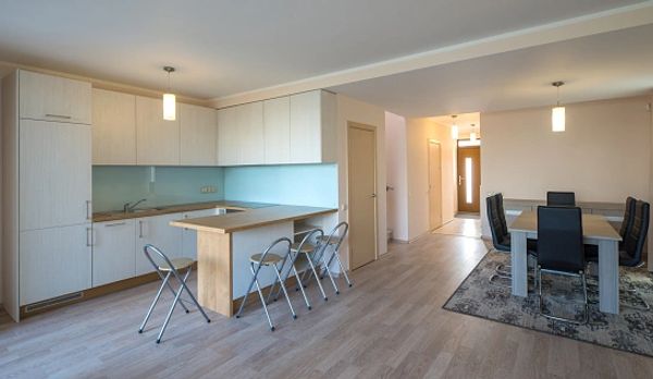 A clean, modern open-plan kitchen and dining area with light wood floors and white cabinets.