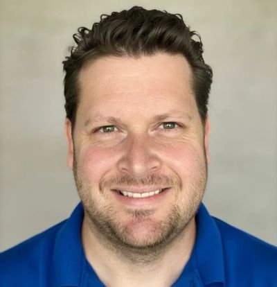 Smiling man with curly hair and a blue shirt.