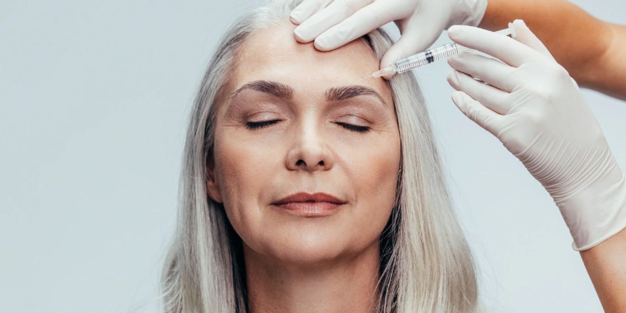 older woman with gray hair receiving an injection above her eyebrow 