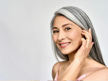 older woman smiling pushing her gray hair behind her ear 
