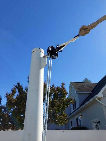 Close-up of a white flagpole with ropes and pulley against a clear blue sky.