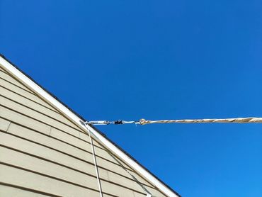 Rope secured to a house roof against a clear blue sky.