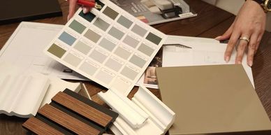 Hands holding a paint swatch and a tile sample with various materials on a table.