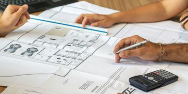 Two people working on architectural plans with a ruler and calculator.
