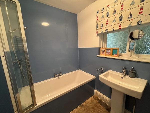Cozy bathroom with blue walls, white bathtub, and sink under a nautical-themed window blind.