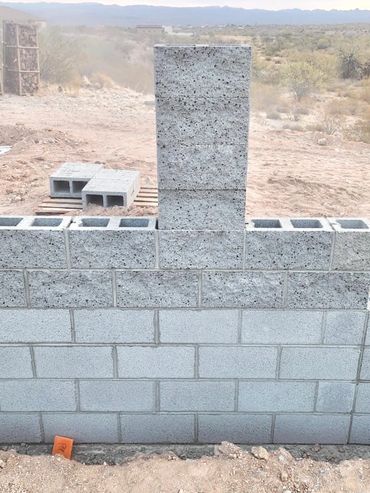 A partially built cinder block wall with a vertical stack of blocks in the center outdoors.