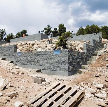 Construction of a terraced retaining wall with concrete blocks on a rocky hillside.