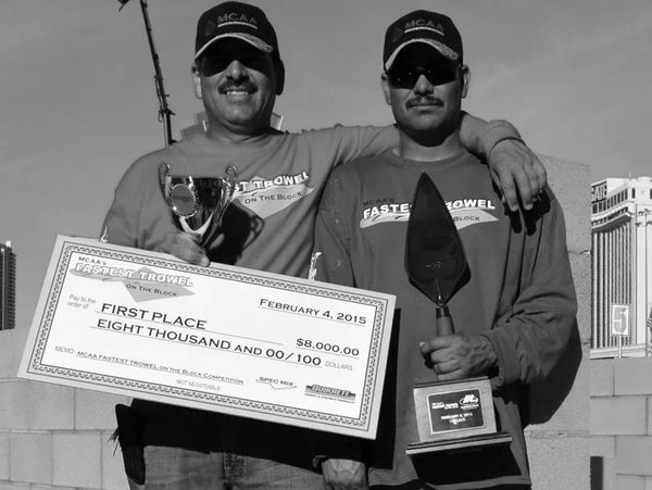 Two men celebrating winning a trowel competition with a trophy and a large check.