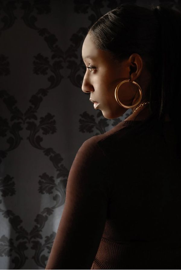 Profile of a woman with gold hoop earrings against patterned wallpaper.