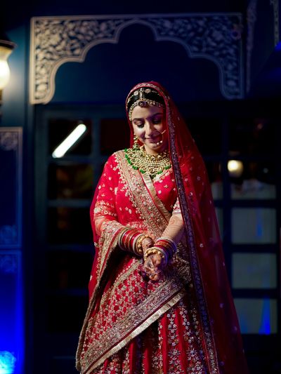 A bride in a traditional red and gold embroidered outfit with jewelry.