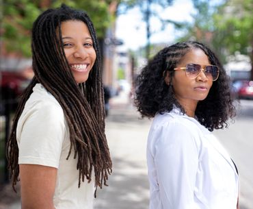 Two women with natural hair outdoors, one smiling and one wearing sunglasses.