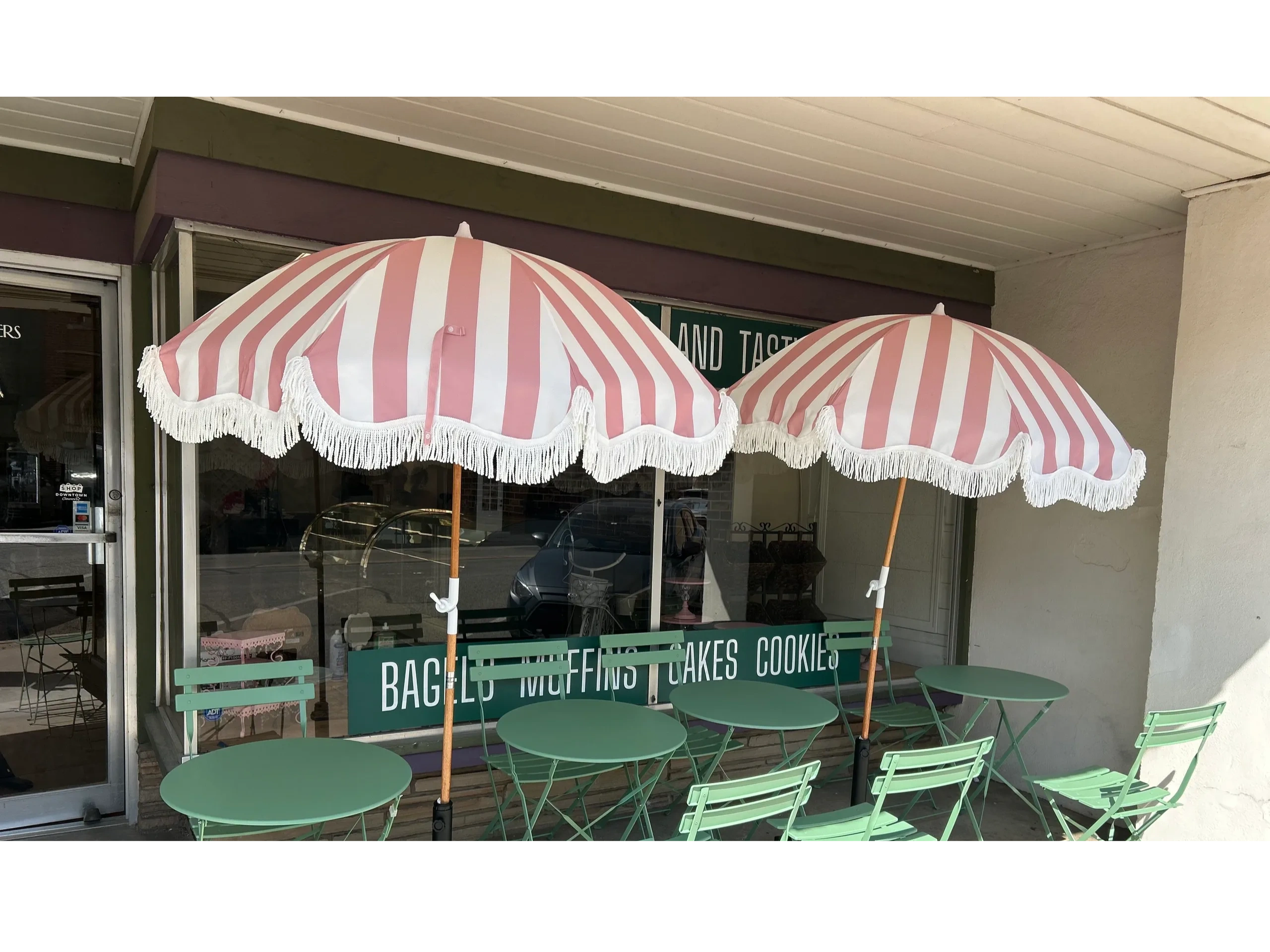 Outdoor cafe seating with pastel green tables, chairs, and pink-striped umbrellas.