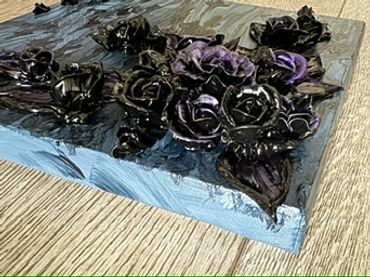 A dark square artwork featuring black roses and deep purple leaves on a textured background