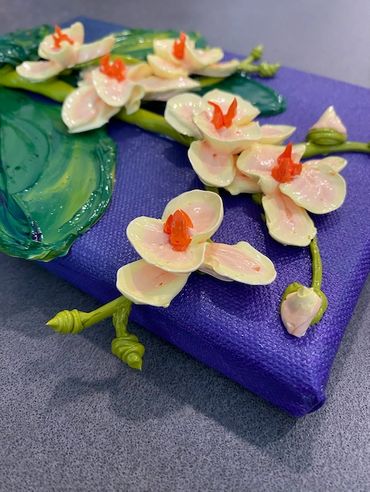 A painting of white orchids with orange centers and green leaves on a dark purple canvas.