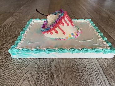 A tilted cake slice with colorful frosting and sprinkles, sitting on a large iced base.
