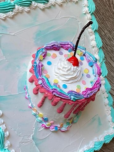 A small round cake with colorful drips, confetti sprinkles, whipped cream, and a cherry.