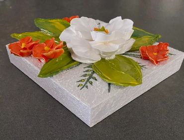 White flower with green leaves, surrounded by smaller orange blooms.