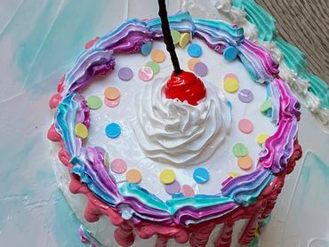 A colorful frosted cake with a whipped cream swirl, cherry, and confetti sprinkles.