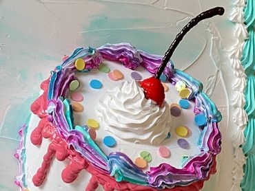 A small round cake with colorful drips, confetti sprinkles, whipped cream, and a cherry.