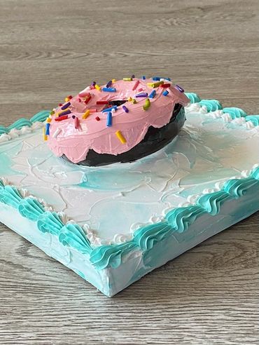 A close-up of a chocolate donut with pink icing, colorful sprinkles, and a frosted base.