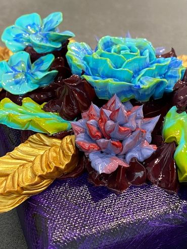 Blue and purple flowers with green and gold leaves on a dark background.