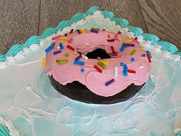 A close-up of a chocolate donut with pink icing, colorful sprinkles, and a frosted base.