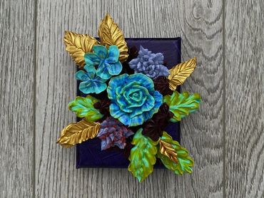 Blue and purple flowers with green and gold leaves on a dark background.
