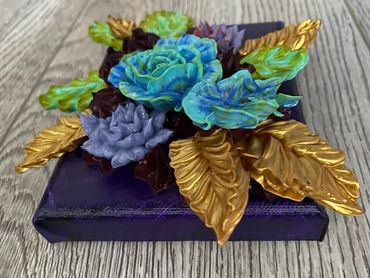 Blue and purple flowers with green and gold leaves on a dark background.