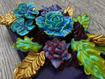 Blue and purple flowers with green and gold leaves on a dark background.