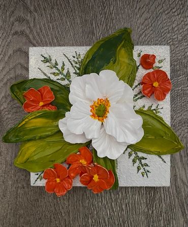 White flower with green leaves, surrounded by smaller orange blooms.