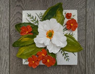 White flower with green leaves, surrounded by smaller orange blooms.