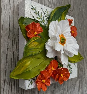 White flower with green leaves, surrounded by smaller orange blooms.