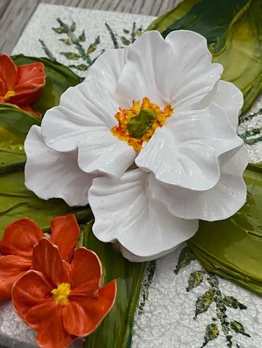 White flower with green leaves, surrounded by smaller orange blooms.